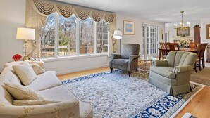 A living room with a sofa, armchairs, a dining table, and a large window with curtains. - Close to Wequaquet Lake, beautiful and spacious cottage (Barnstable)