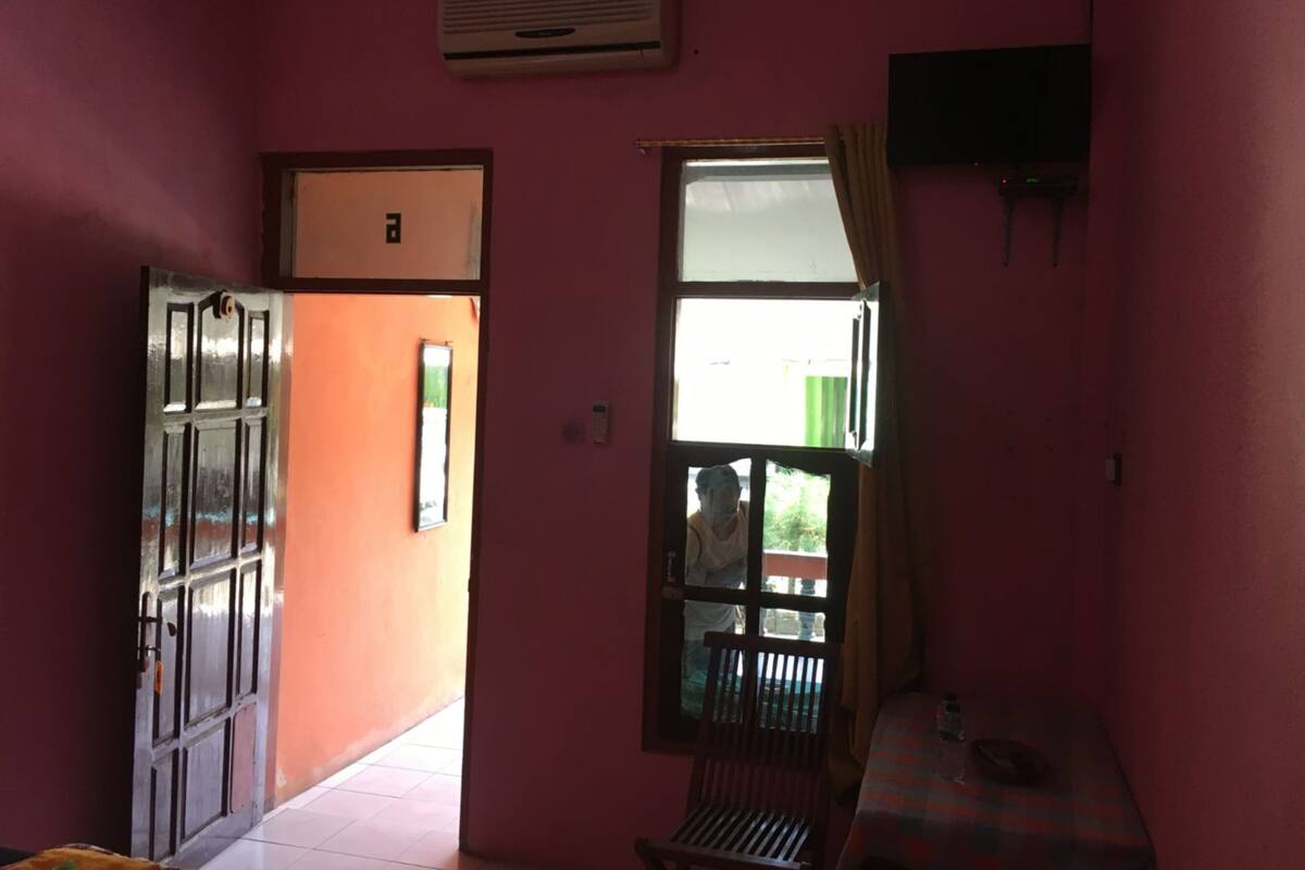 Una habitació amb parets roses, una finestra amb cortines, una taula amb una ampolla i una porta que dona a l'exterior.