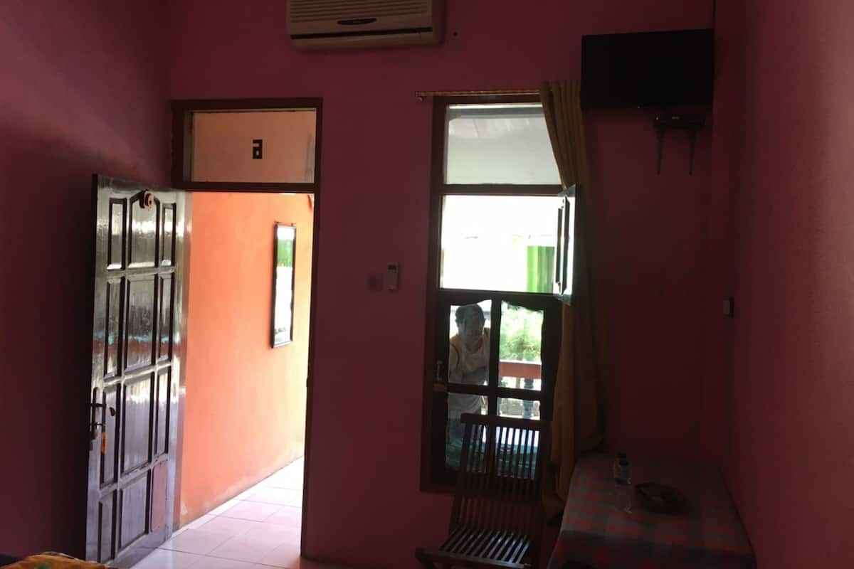 Una habitación con paredes rosas, una ventana con cortinas, una mesa con una botella y una puerta que da al exterior.