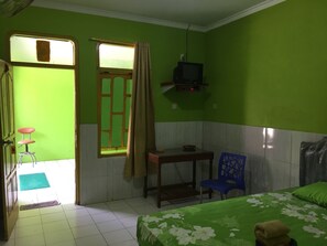 A small, green-walled room with a bed, a chair, a table, a television, and a window with curtains. - Hotel Trias Parangtritis by Zuzu (Parangtritis)