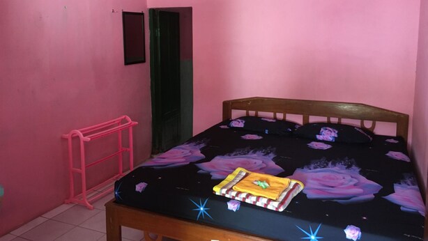 A small, pink-walled room with a wooden bed, a pink ladder, and a green door. - Hotel Trias Parangtritis by Zuzu (Parangtritis)