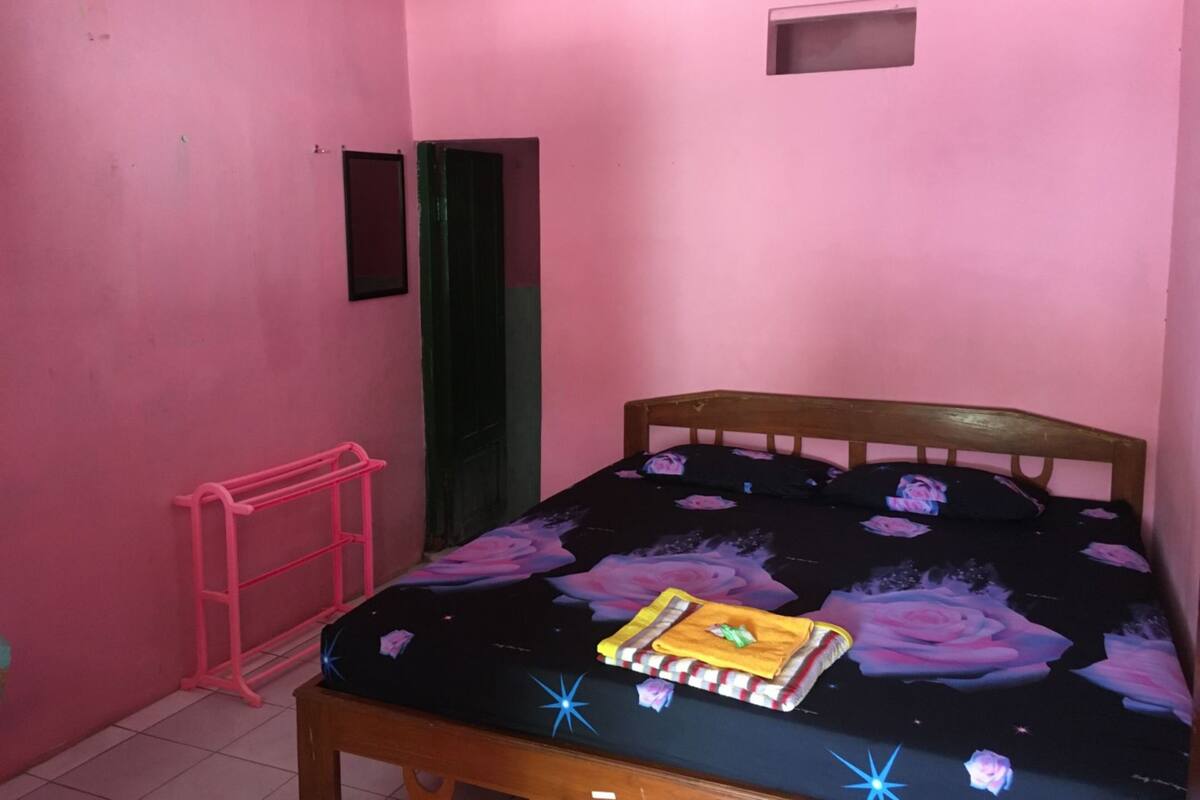 Una habitació petita amb parets roses, un llit de fusta, una escala rosa i una porta verda.