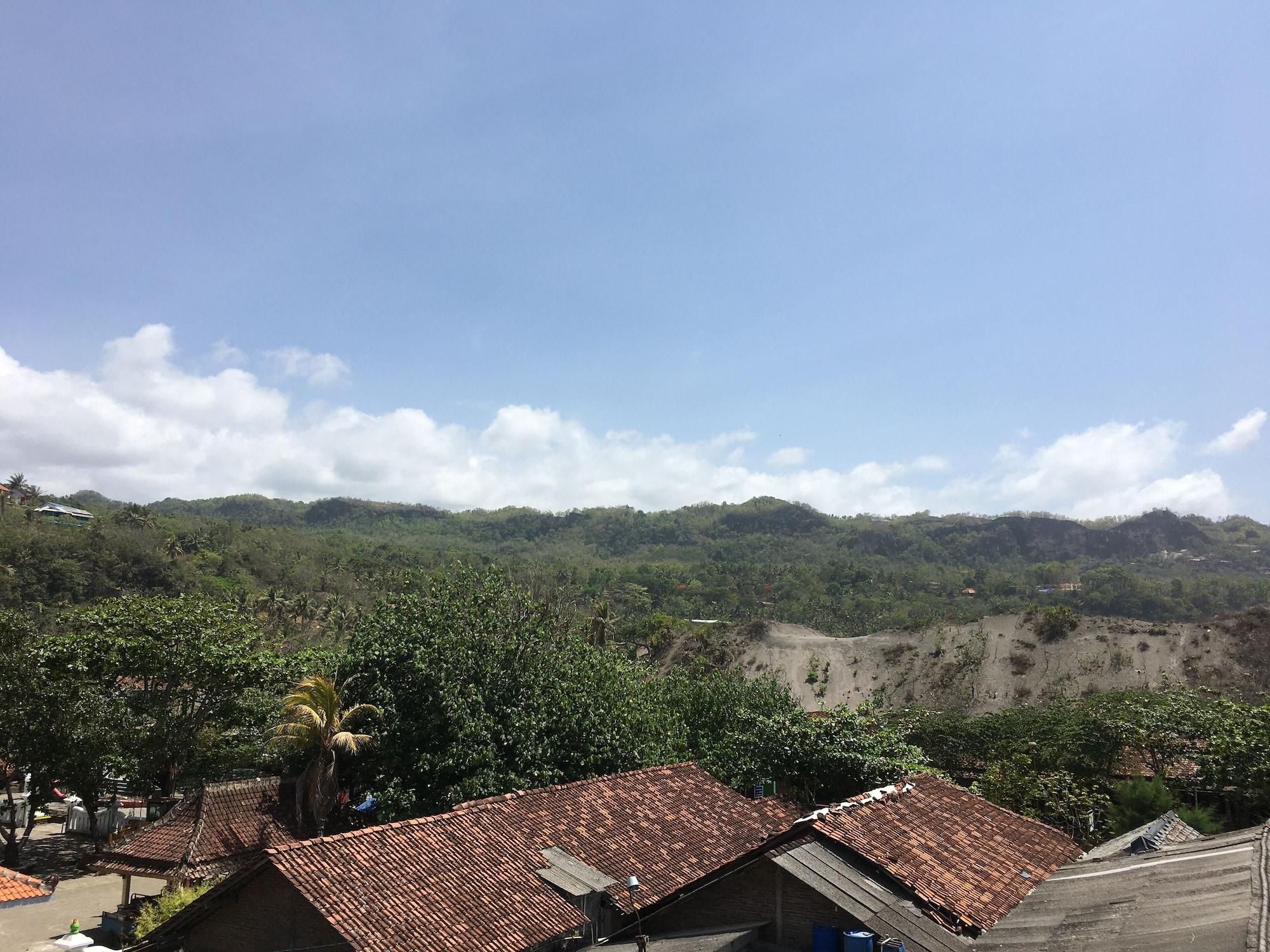 A residential area with houses featuring red-tiled roofs, surrounded by lush greenery and hills in the background.