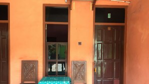 A building with two wooden doors, a bench with a green patterned tablecloth, and a tiled floor. - Hotel Trias Parangtritis by Zuzu (Parangtritis)