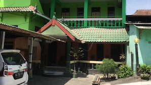 A multi-story building with a green facade, a covered entrance, and a parked car in front. - Hotel Trias Parangtritis by Zuzu (Parangtritis)