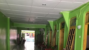 A corridor with green walls, tiled flooring, and wooden chairs with red tablecloths. - Hotel Trias Parangtritis by Zuzu (Parangtritis)