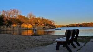 Un banc au bord d’une rivière paisible, avec des arbres aux couleurs automnales en arrière-plan.