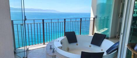 A balcony with a jacuzzi tub, glass doors, and a view of the sea.