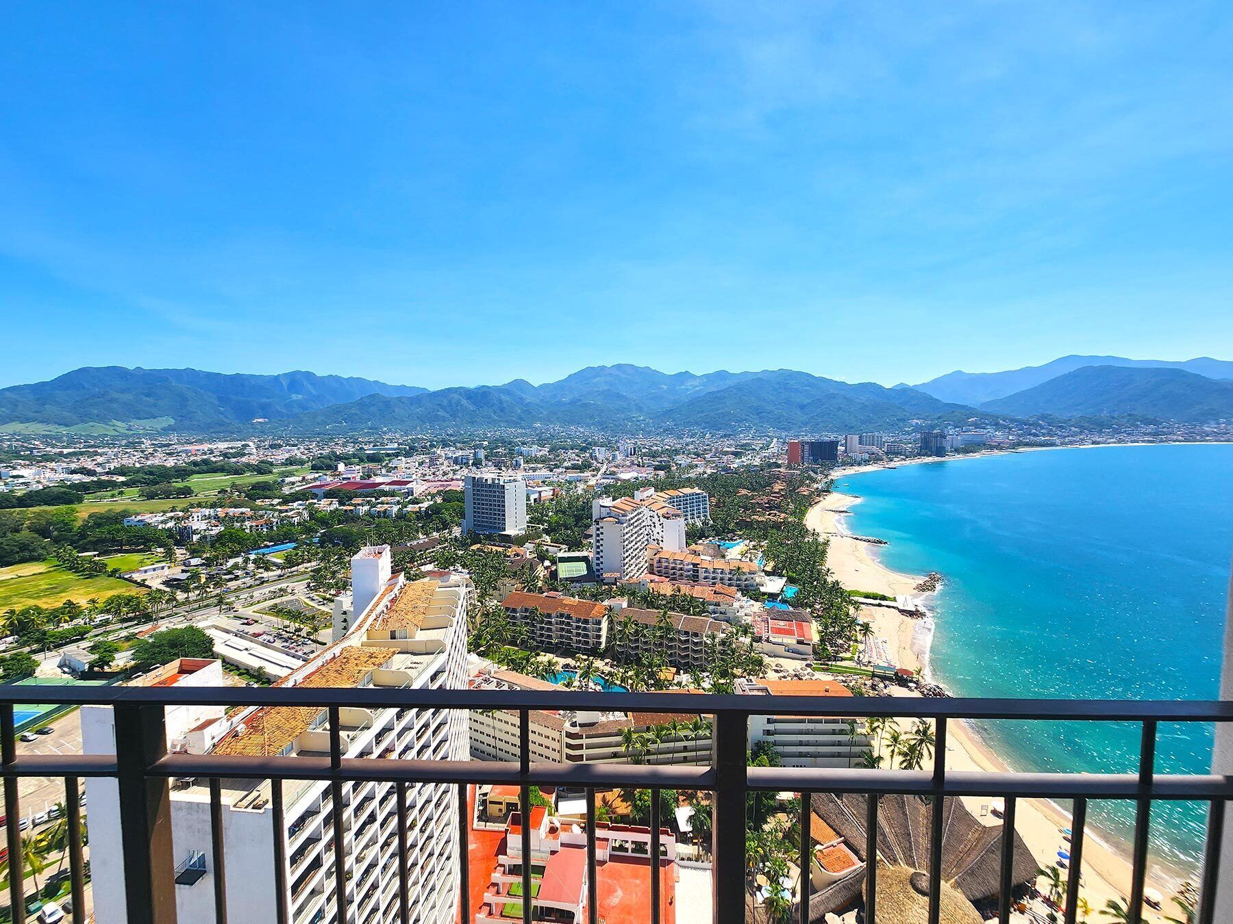 A coastal cityscape with a beach, mountains, and a mix of residential and commercial buildings.