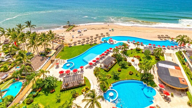 A resort with a large swimming pool, beach, and palm trees.