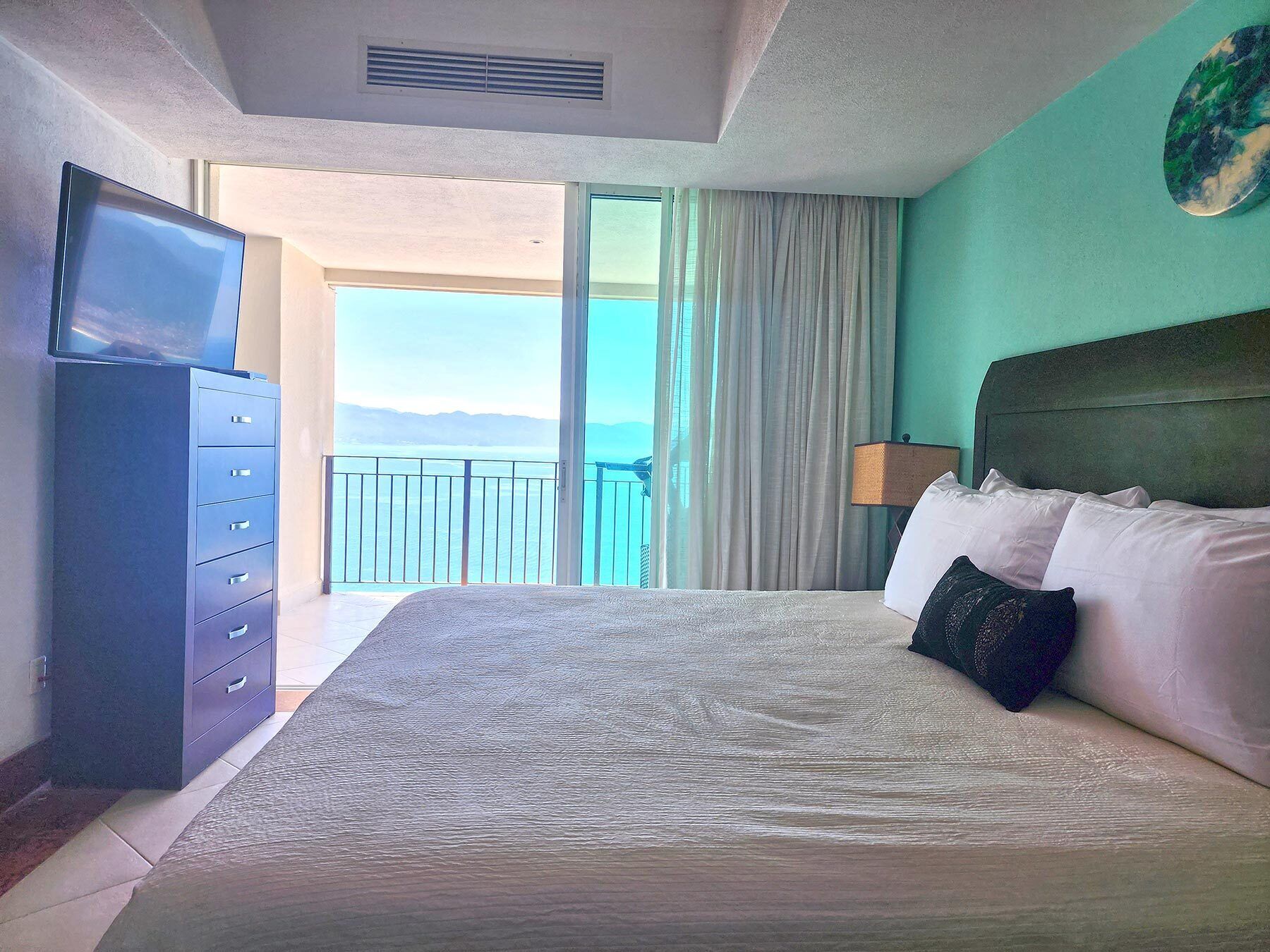 Quarto de hotel com uma cama grande, televisão em uma cômoda e varanda com vista para o mar.