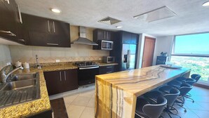 A modern kitchen with dark cabinets, granite countertops, stainless steel appliances, and a bar area with stools.