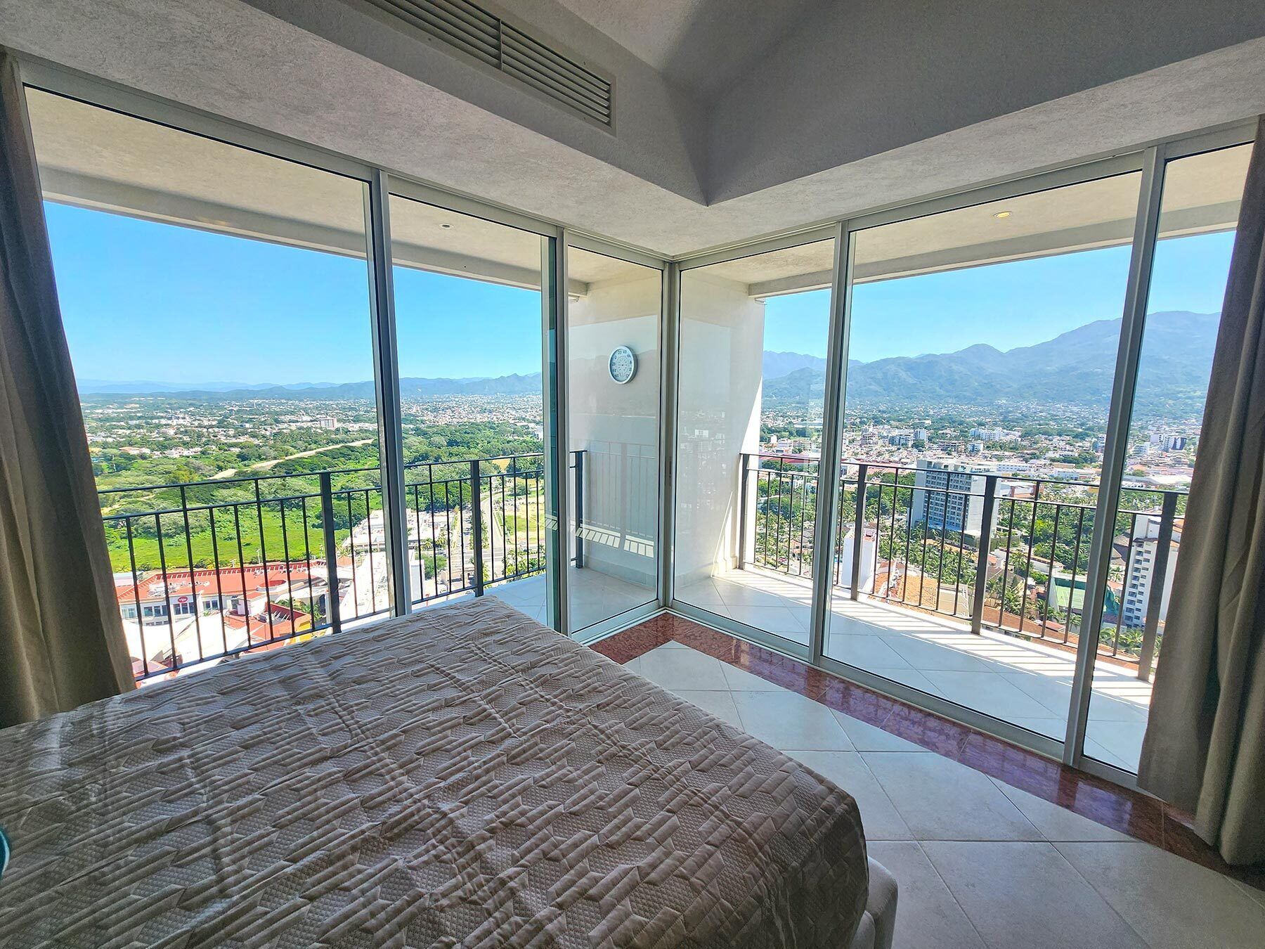 A spacious balcony with a bed, large windows, and a city view.