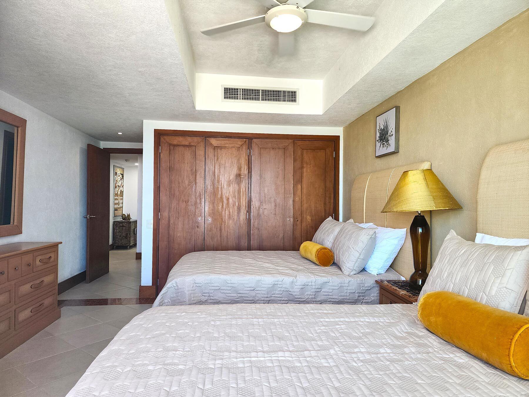 A bedroom with two beds, a ceiling fan, a nightstand with a lamp, and a wooden wardrobe.