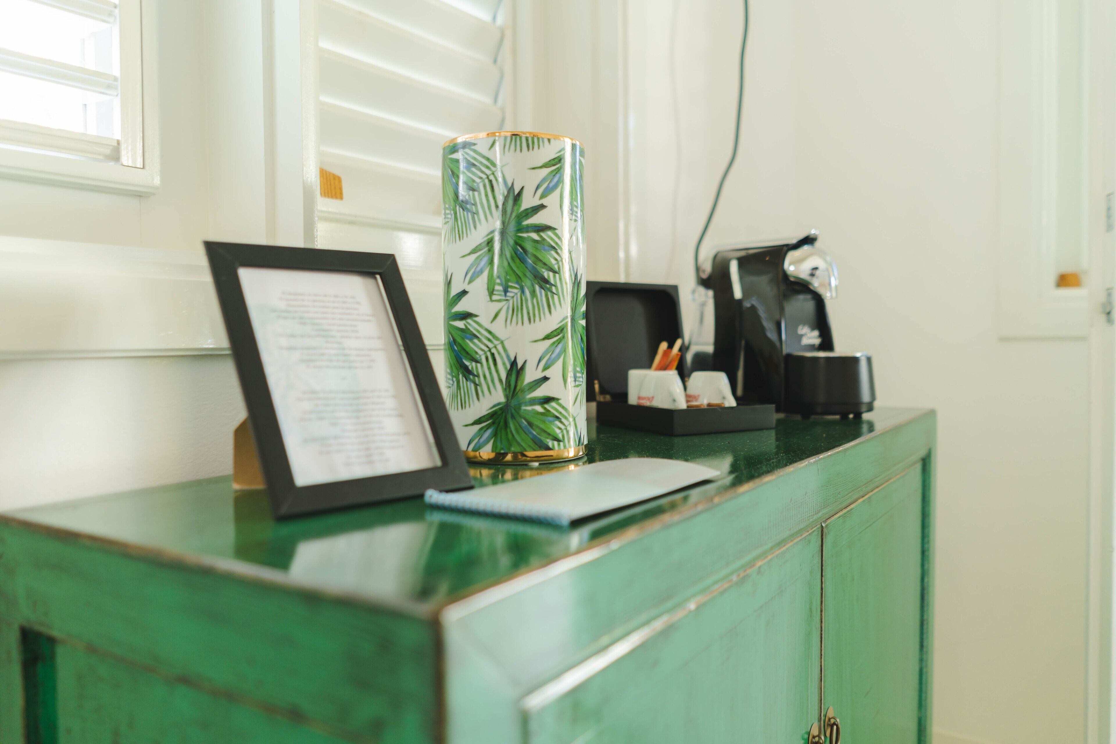 A reception desk with a framed menu, a decorative vase, a coffee machine, and a green cabinet.