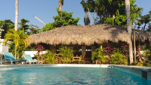 A pool area with lounge chairs, a thatched-roof structure, and tropical vegetation. - Punta Popy Boutique Hotel (Las Terrenas)