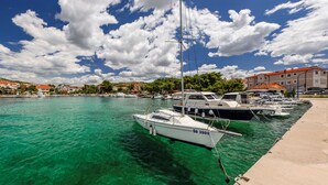 Un port de plaisance avec des bateaux amarrés, une eau turquoise et limpide, et des bâtiments aux toits rouges en arrière-plan.