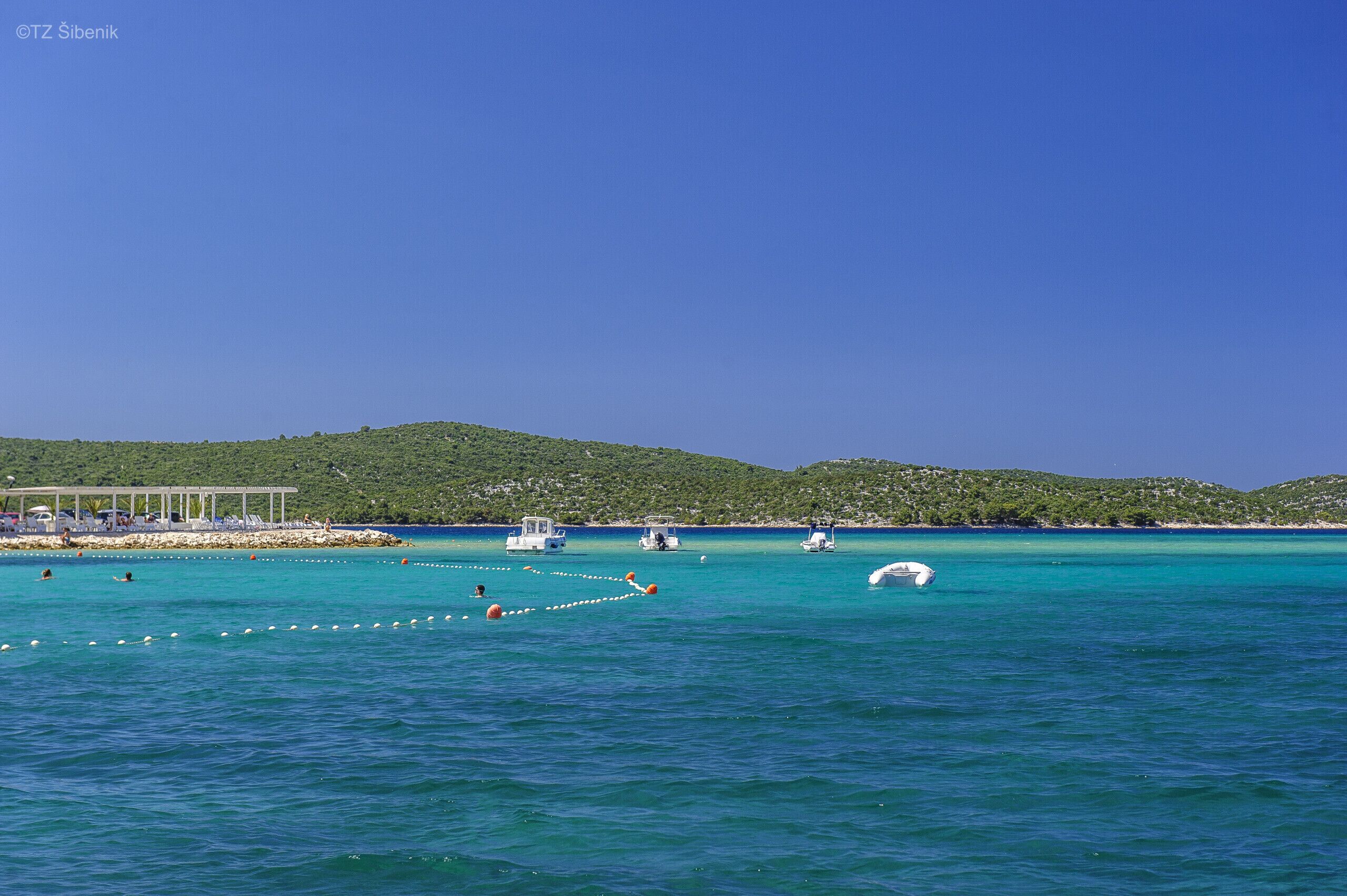 Eine Küstenlandschaft mit einem Steg, Booten und blauem Himmel.