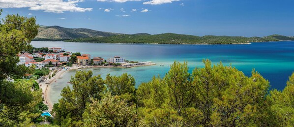 A coastal town with buildings along the waterfront, a beach, and a clear view of the sea and hills in the background. - Apartments Marijana Žaborić - sea view A1 (Žaborić)