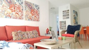 Un salon avec un canapé rouge, un fauteuil en osier avec un coussin bleu et une table basse sur laquelle se trouve un bol.