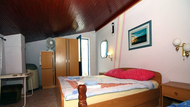 A bedroom with a wooden bed, a desk, a wardrobe, and a ceiling fan. - Holiday Home Serov - four bedroom house (Tisno)