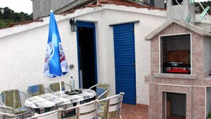 An outdoor patio with a table and chairs, a barbecue grill, and a blue door. - Holiday Home Serov - four bedroom house (Tisno)
