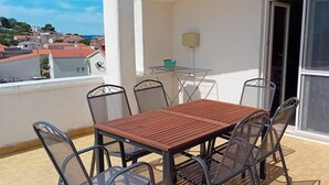 A balcony with a wooden table and metal chairs, a small glass table with a basket, and a view of the town. - Apartments Alaga - B4+2 (Tribunj)