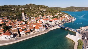 Un pueblo costero con una torre destacada, un puente y un puerto deportivo con barcos.