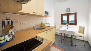 Cocina compacta con estufa, microondas y lavamanos. Hay una mesa de comedor con sillas y una ventana con vistas.