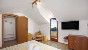 Een slaapkamer met een bed, een televisie, een houten kast en uitzicht op zee.