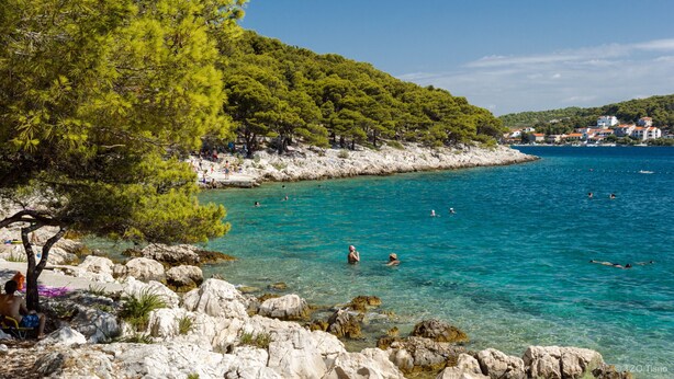 Een kustgebied met helder turquoise water, rotsachtige oevers en een achtergrond van weelderige groene heuvels.