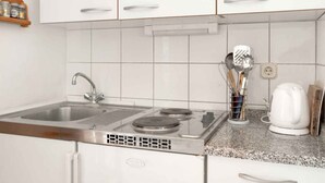 A kitchen with white cabinets, a stainless steel sink, a built-in stove, and a kettle on the countertop. - Apartments Maretic Brodarica A1 (Šibenik-Brodarica)