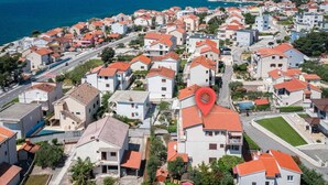 A coastal residential area with houses featuring red-tiled roofs, a prominent red location marker, and a view of the sea. - Apartments Maretic Brodarica A1 (Šibenik-Brodarica)
