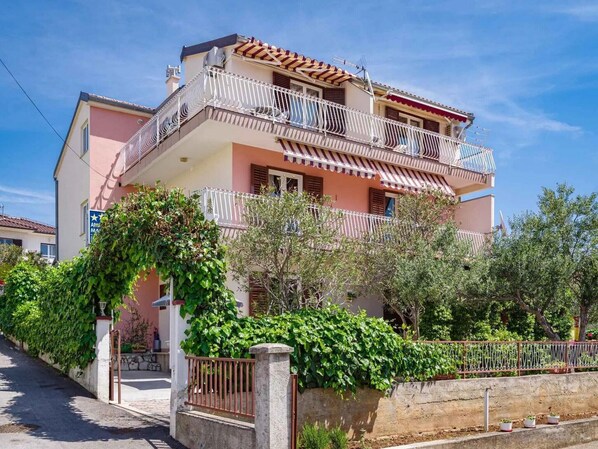 A multi-story residential building with balconies, a gated entrance, and surrounding greenery.