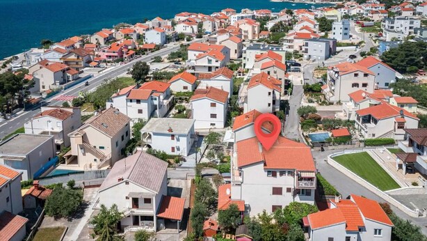 A coastal residential area with houses featuring red-tiled roofs, a prominent red location marker, and a view of the sea. - Apartments Maretic Brodarica A2 (Šibenik-Brodarica)