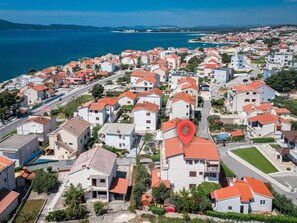 A coastal residential area with houses featuring red-tiled roofs, a prominent red location marker, and a view of the sea.