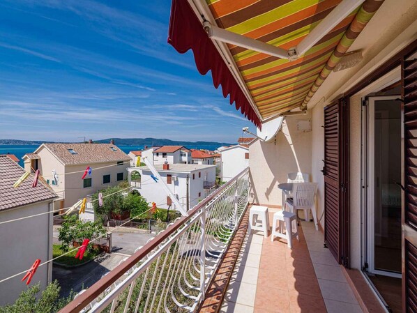 A balcony with a view of the sea, white chairs, and a striped awning.
