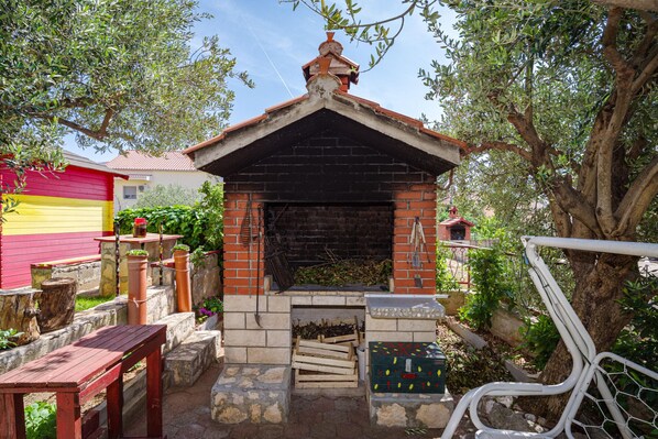 A brick-built outdoor barbecue area with a chimney, surrounded by stone steps and potted plants.