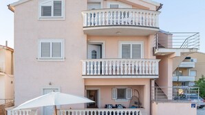Un immeuble à plusieurs étages doté de balcons, d’une cour pavée de pierres et d’un parasol blanc.