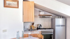 Une cuisine compacte dotée de meubles en bois, d’une cuisinière à gaz, d’un réfrigérateur en acier inoxydable et d’une petite table à manger avec des chaises.
