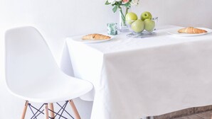 A dining table with a white tablecloth, a vase with flowers, a bowl of green apples, and a croissant on a plate. - Apartments Nikol Vodice - sea view A5 (Vodice)
