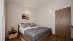 A bedroom with a bed, bedside table, lamp, and a wooden wardrobe. - Beachfront One Bedroom Apartment Savin (Šibenik-Brodarica)