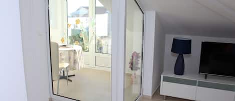 A modern living room with a glass door leading to a balcony, a flat-screen TV, and a decorative vase.