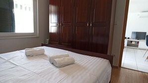 A bedroom with a large bed, wooden wardrobe, and a window with curtains.