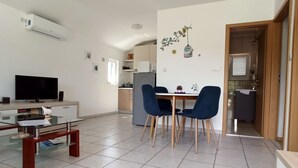 A modern living room with a glass coffee table, a flat-screen TV, and a dining area with blue chairs.