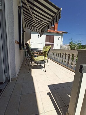 Un balcon doté d’un sol carrelé, d’une table avec des chaises et d’une rambarde blanche.