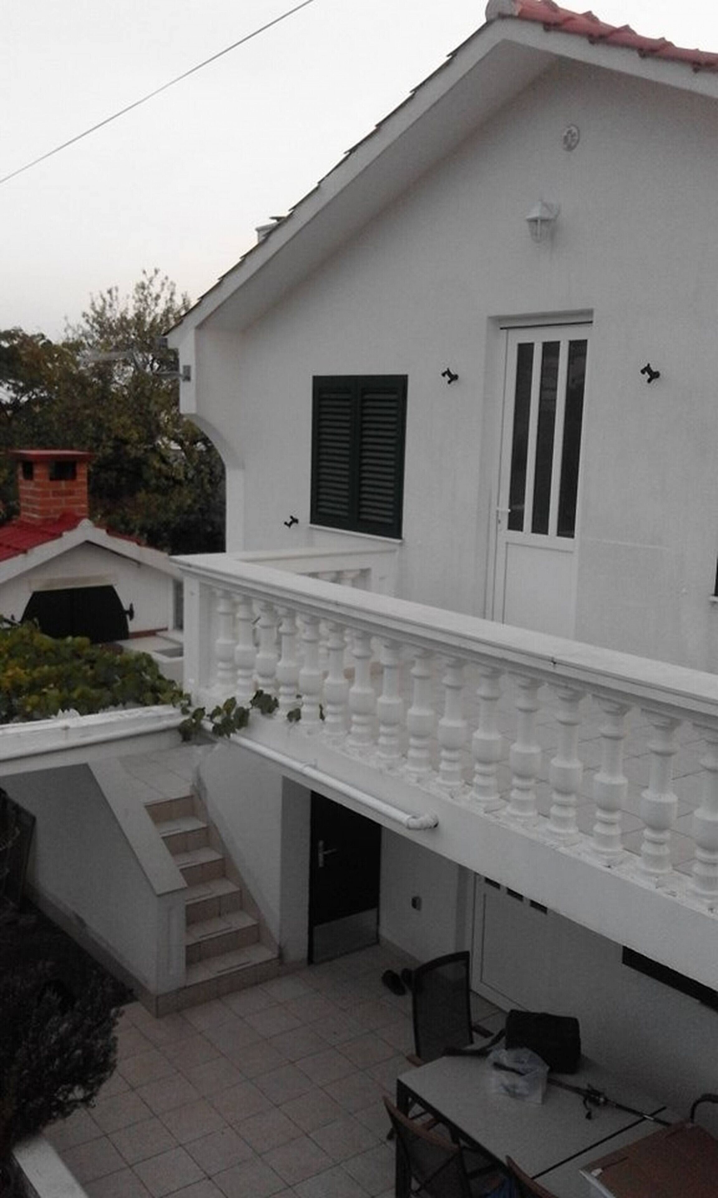 A two-story building with a white exterior, a balcony with balusters, a door, and a window with shutters.