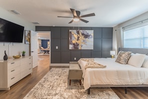 A modern bedroom with a bed, a ceiling fan, a TV, and a large abstract painting on the wall.
