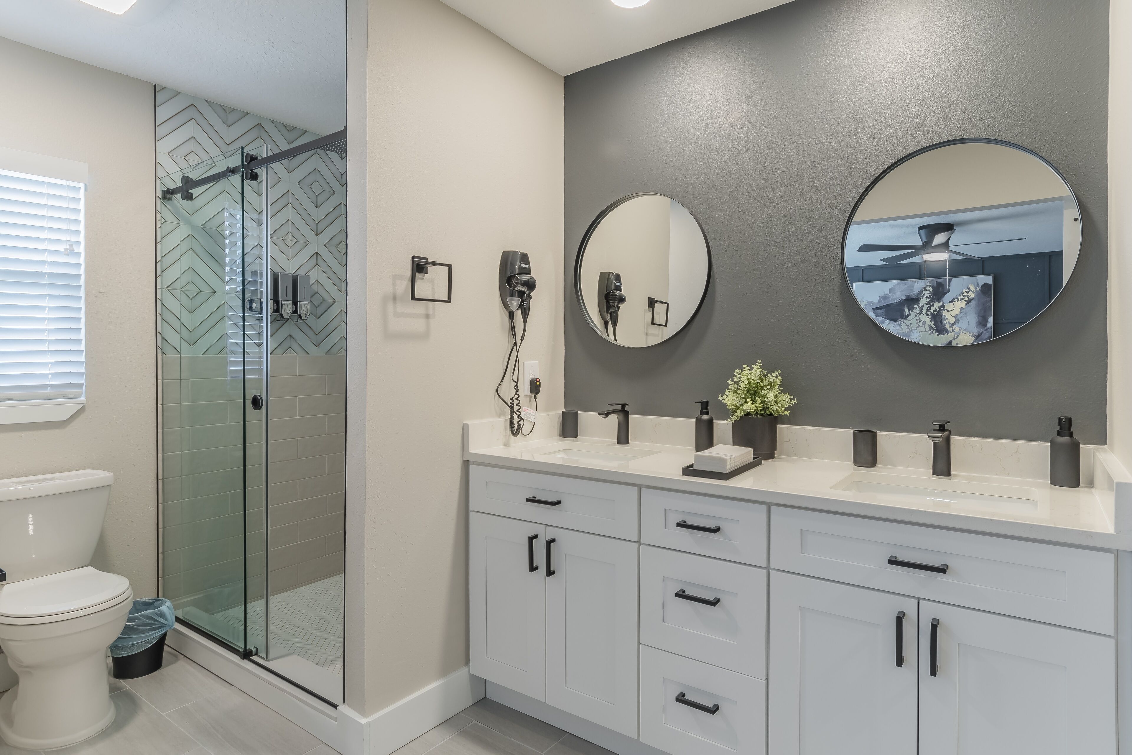 A modern bathroom with a glass shower enclosure, a white toilet, and a vanity with a mirror and two sinks.