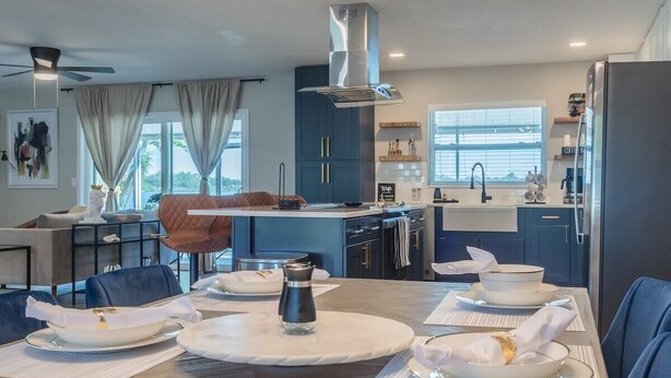 Une cuisine moderne avec un coin repas, comprenant un grand îlot central, des meubles de couleur bleu foncé et une hotte de cuisine en acier inoxydable.